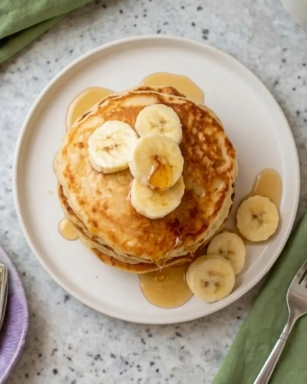 Overhead view of a plate of banana cottage cheese pancakes topped with banana slices and syrup