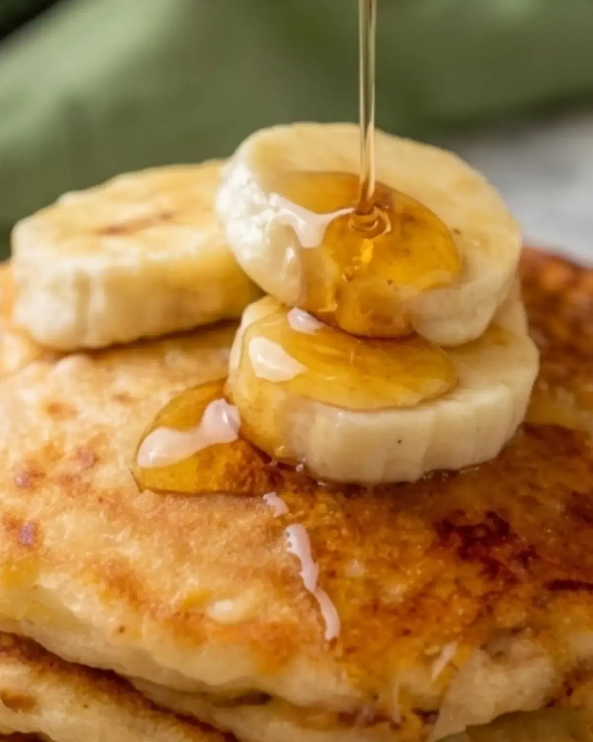 Close-up of banana cottage cheese pancakes topped with banana slices and honey syrup