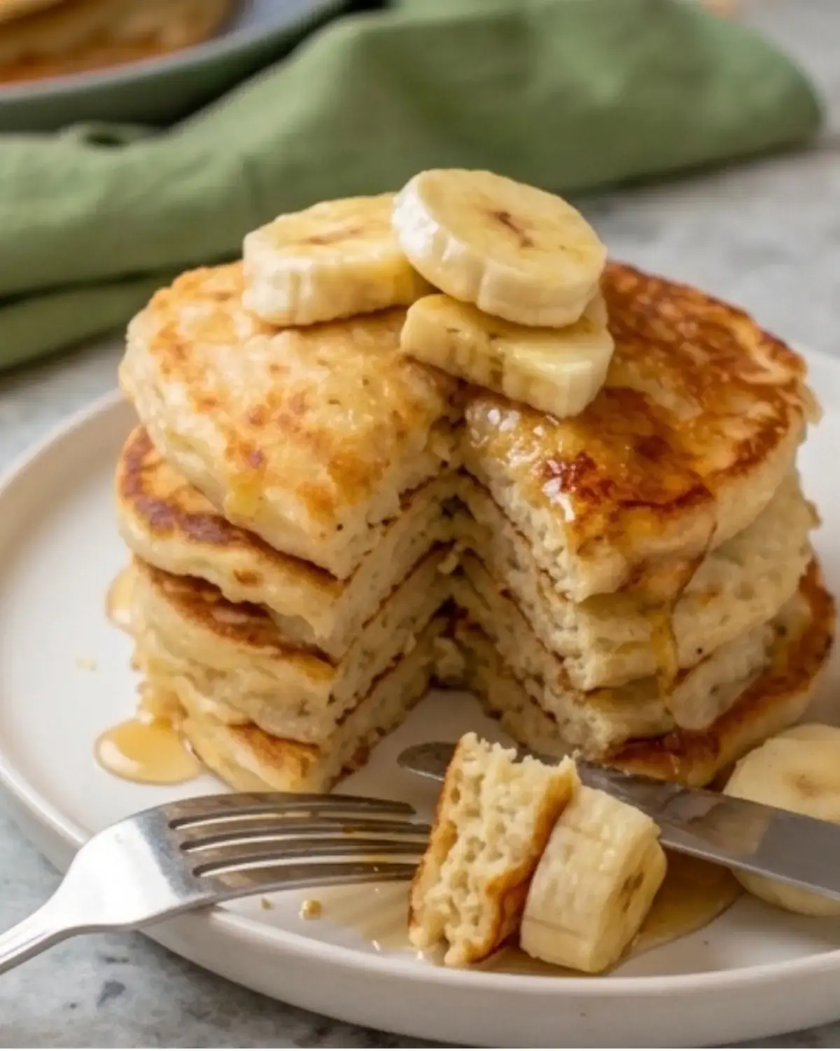 Cut stack of banana cottage cheese pancakes showing the fluffy inside with banana slices on top