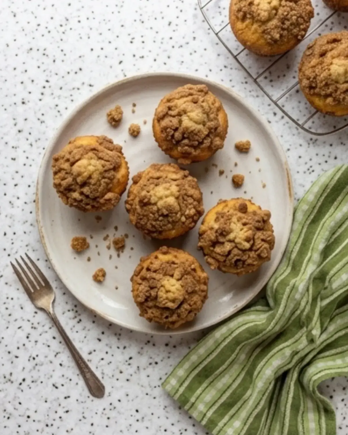 Plate of cinnamon streusel muffins with crumb topping on a speckled counter